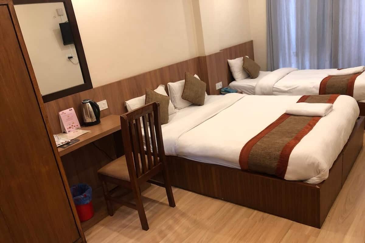 A hotel room with two beds, a desk with a chair, a small trash bin, and a mirror.