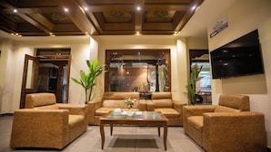 A spacious living area with a brown leather sofa set, a glass coffee table, and a flat-screen TV mounted on the wall. - Capital Boutique Hotel (Kathmandu)