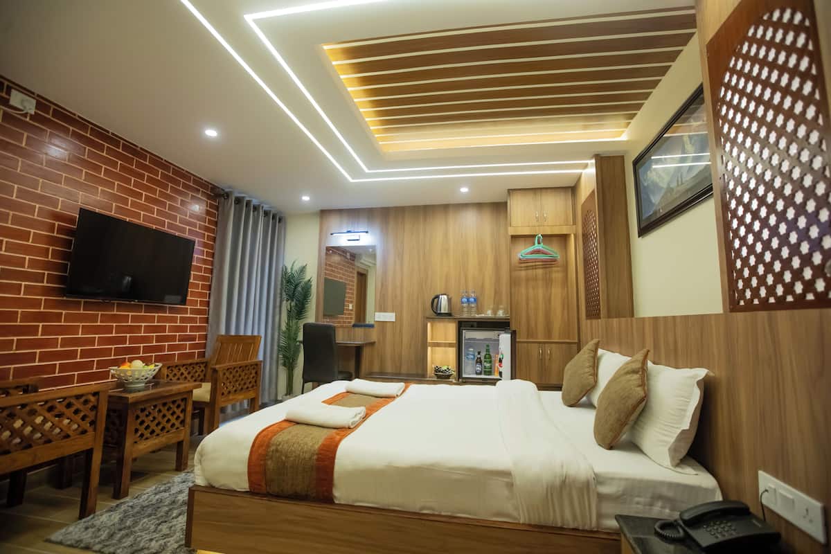 A hotel room with a brick wall, wooden furniture, a flat-screen TV, a bed with white linens, a desk with a chair, and a small refrigerator.
