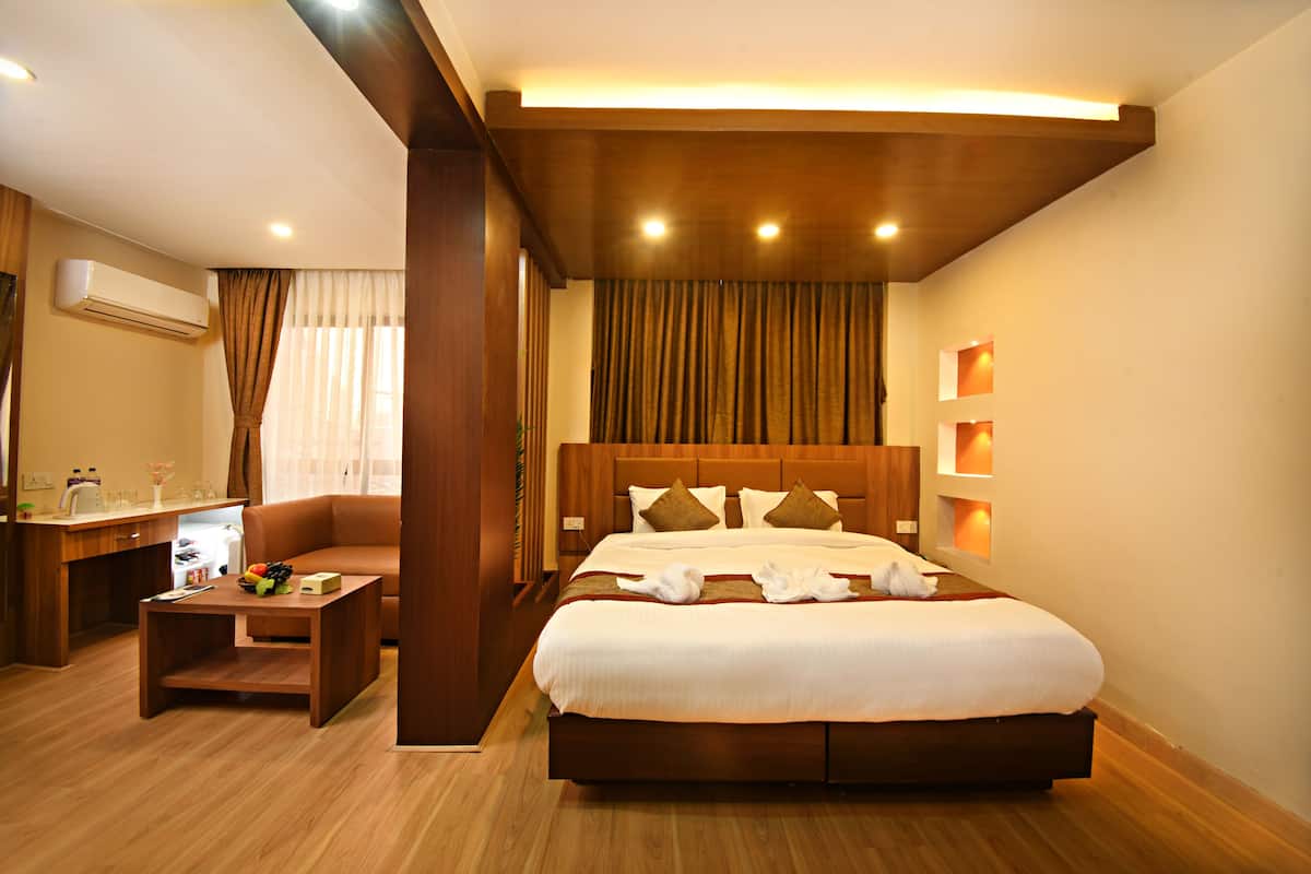 A hotel room with a large bed, a wooden desk, a small table with fruit, and a TV.