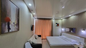 A modern hotel room with a bed, a sofa, a TV, and a painting on the wall. - Black Sea Apartments Alliance Palace (Batumi)