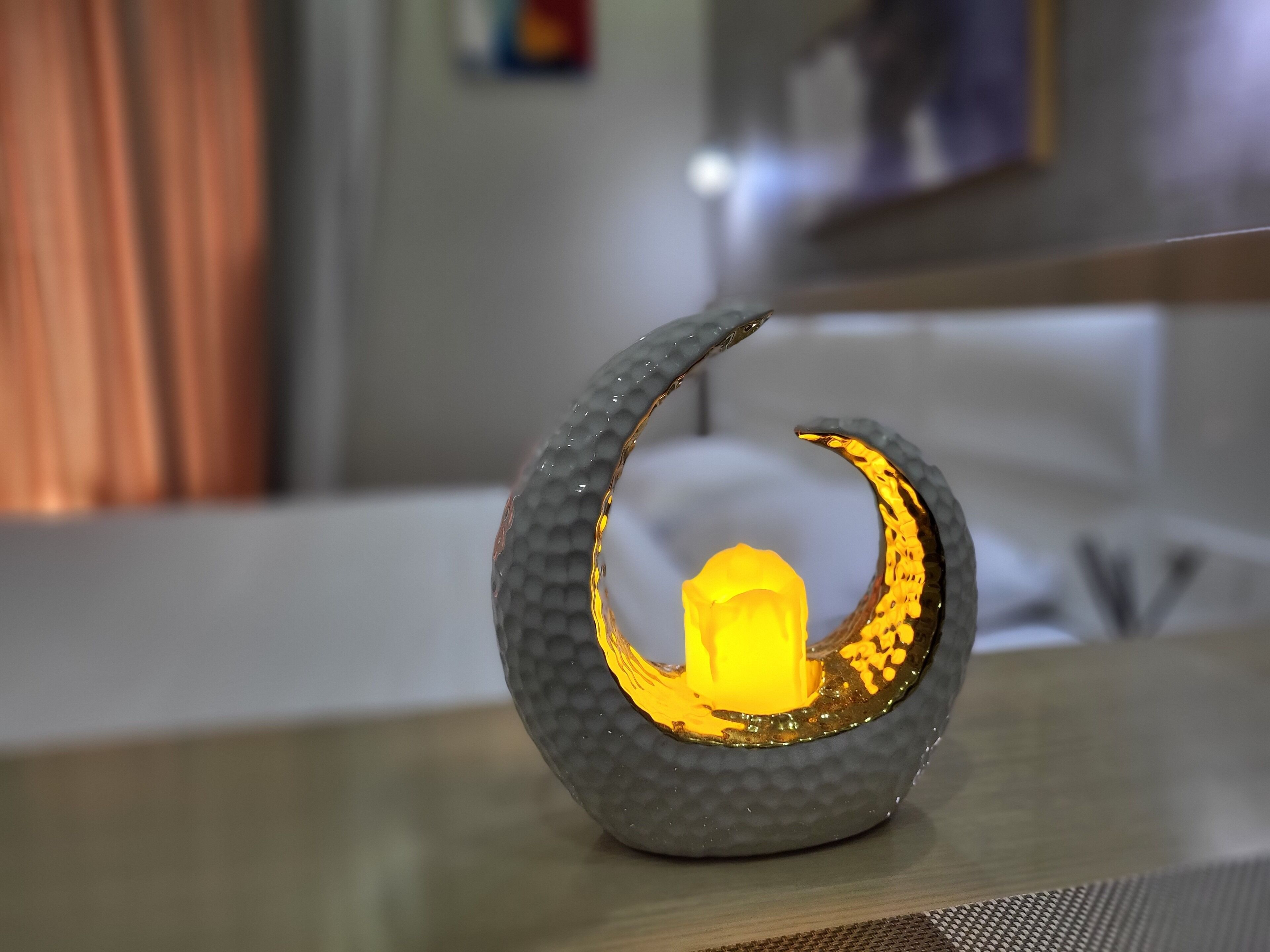 Ein dekoratives Objekt in Form eines Halbmonds mit einem leuchtenden Element in der Mitte, platziert auf einem Tisch in einem Raum mit unscharfem Hintergrund.