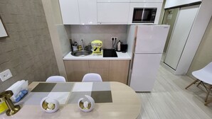 A compact kitchen with a sink, microwave, and refrigerator. There is a dining table with chairs and a small rug. - Black Sea Apartments Alliance Palace (Batumi)