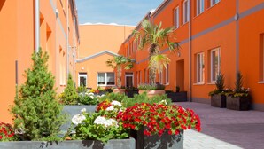 A courtyard with orange buildings, potted plants, and a palm tree. - Winrooms (Wiener Neustadt)