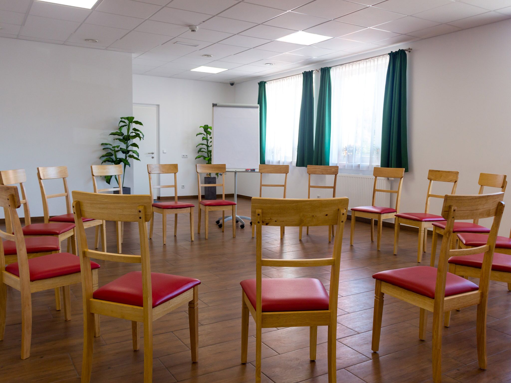 A conference room with wooden chairs and a whiteboard, large windows with curtains, and a potted plant.
