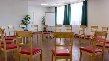 A conference room with wooden chairs and a whiteboard, large windows with curtains, and a potted plant.