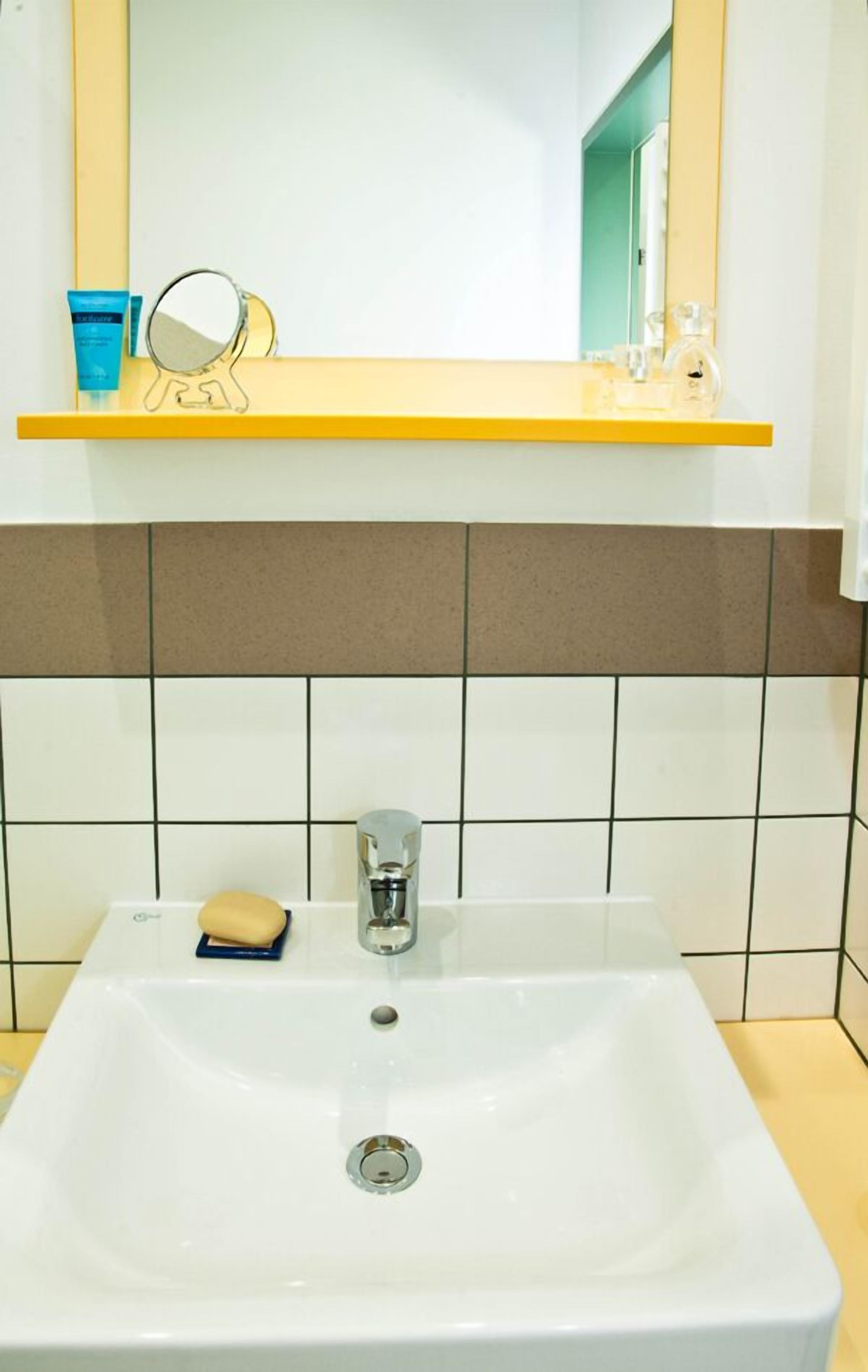 Un baño con un lavabo blanco, un espejo y un estante con artículos de aseo.