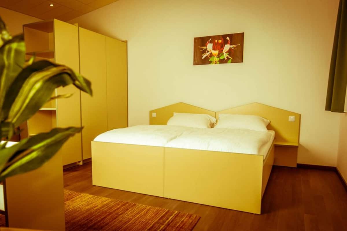 A modern hotel room with a large bed, a potted plant, and a painting on the wall.