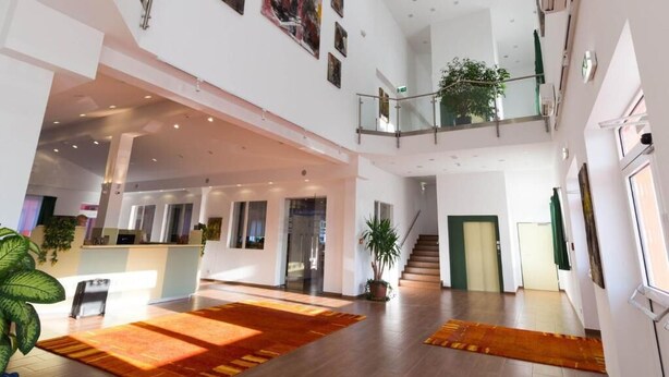 A spacious, multi-level hotel lobby with a reception desk, a staircase, and a large plant. - Winrooms (Wiener Neustadt)