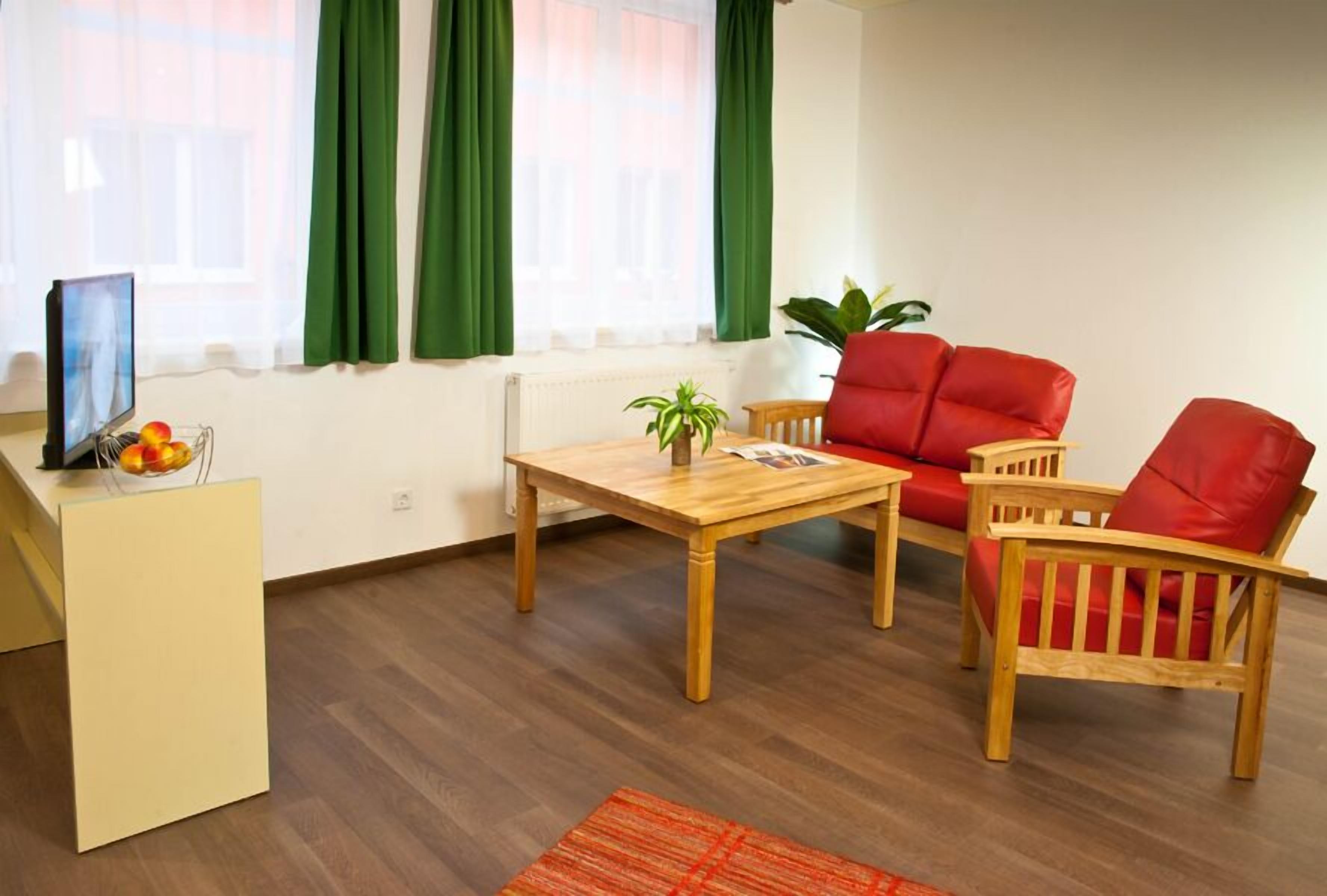 Una sala de estar con una mesa de madera, dos sillas rojas, una planta pequeña y un radiador.