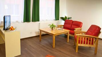 Una sala de estar con una mesa de madera, dos sillas rojas, una planta pequeña y un radiador.