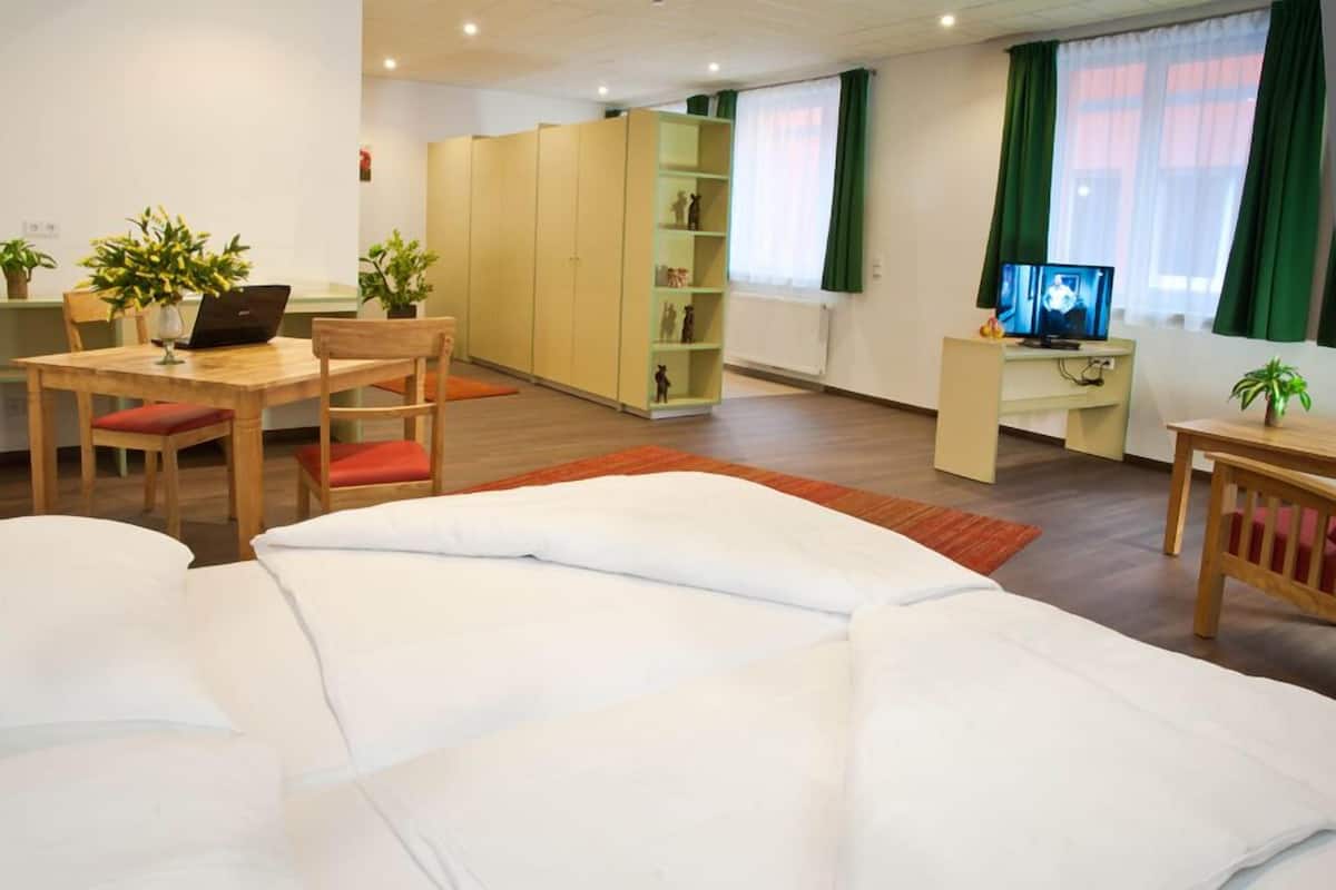 A hotel room with a bed, a desk with a laptop, a television, and a bookshelf.
