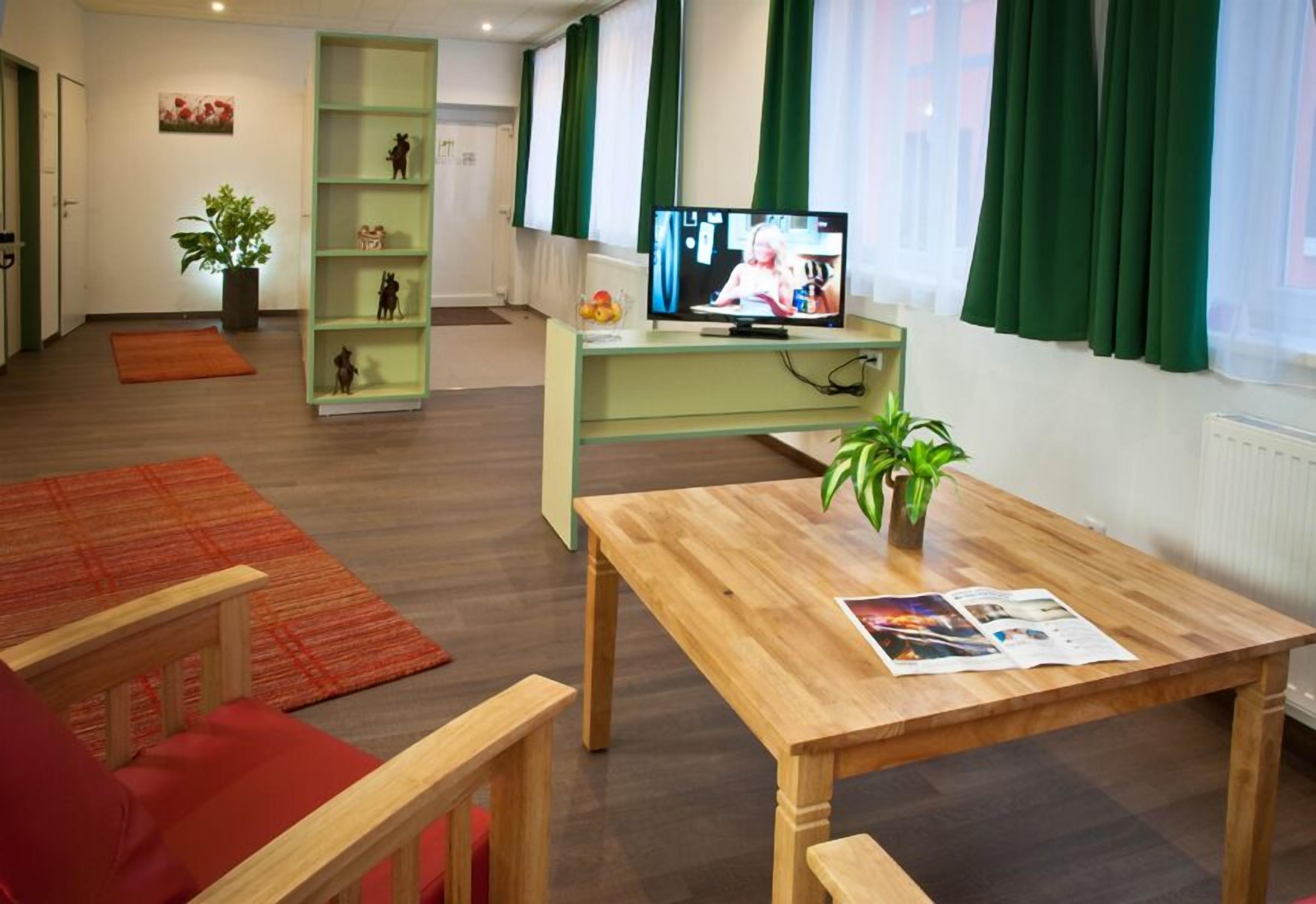 A modern living room with a wooden coffee table, a green shelving unit, and a television.