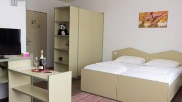 A bedroom with a bed, a desk, a television, and a shelf with a panda plush toy.