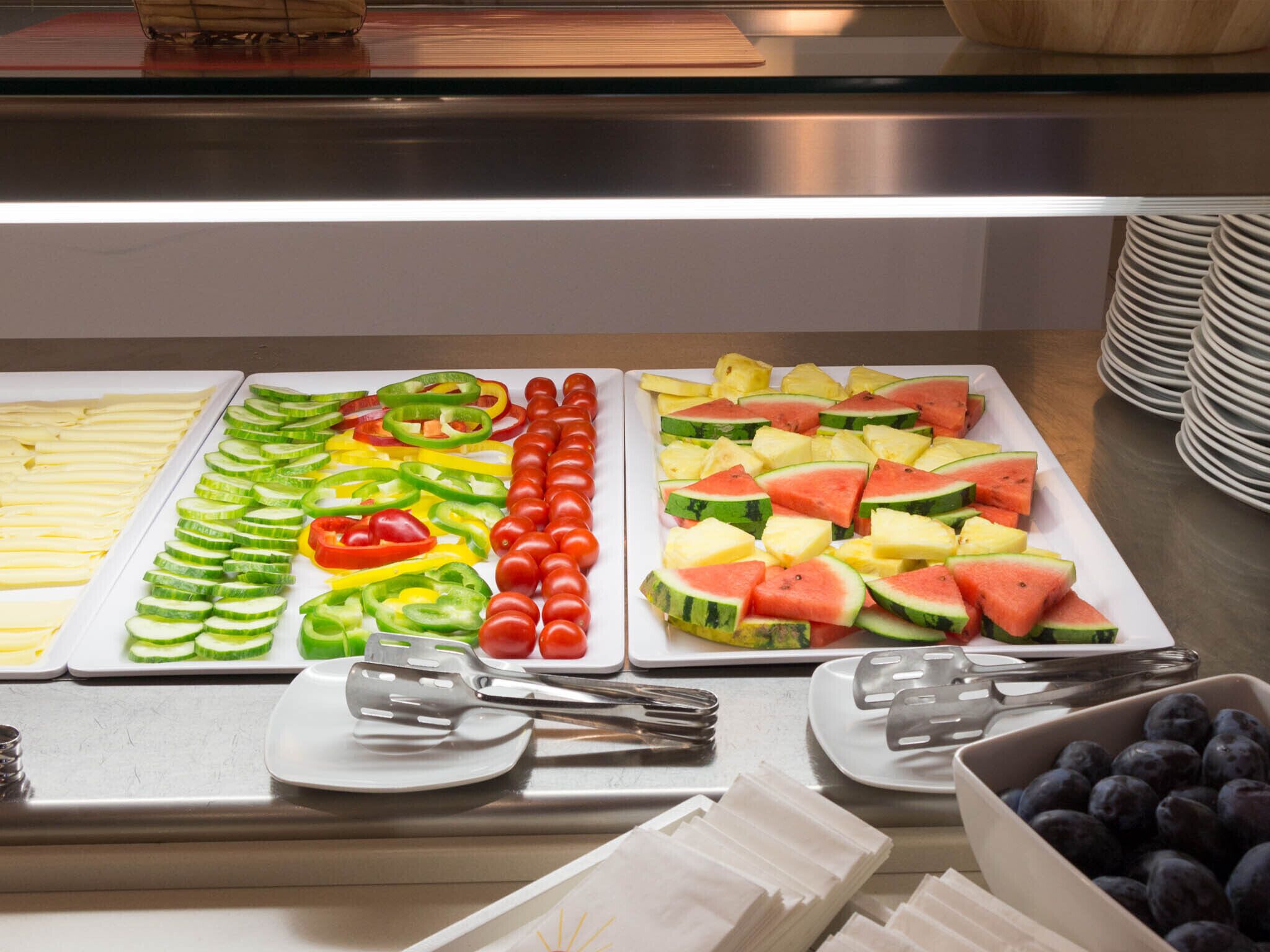 Un bufé con diversas frutas y verduras, incluyendo pepinos, tomates y sandía, dispuestas en platos.