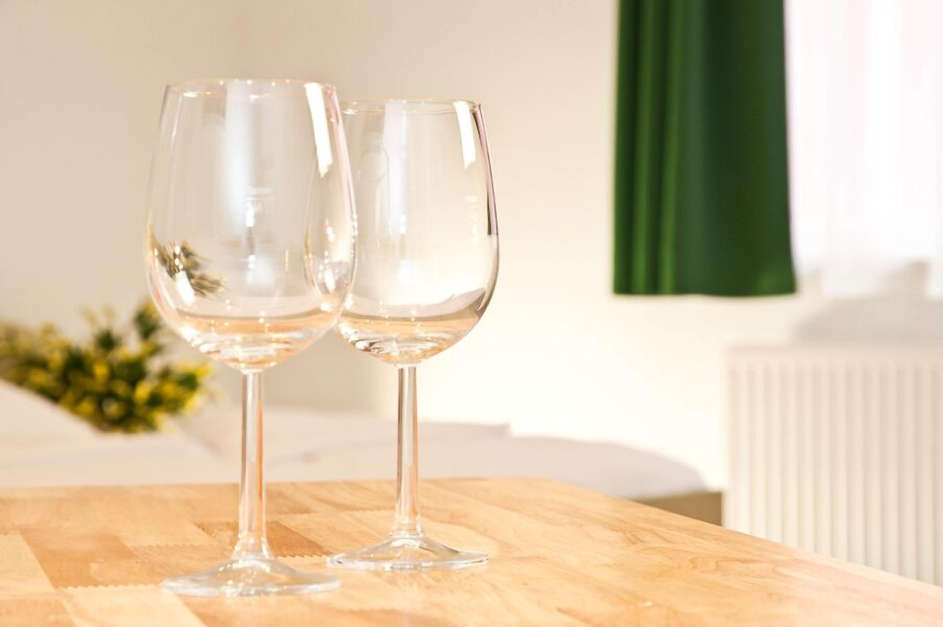 Dos copas de vino vacías sobre una mesa de madera en una habitación con un radiador y una cortina verde al fondo.