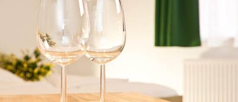 Two empty wine glasses on a wooden table in a room with a radiator and a green curtain in the background.