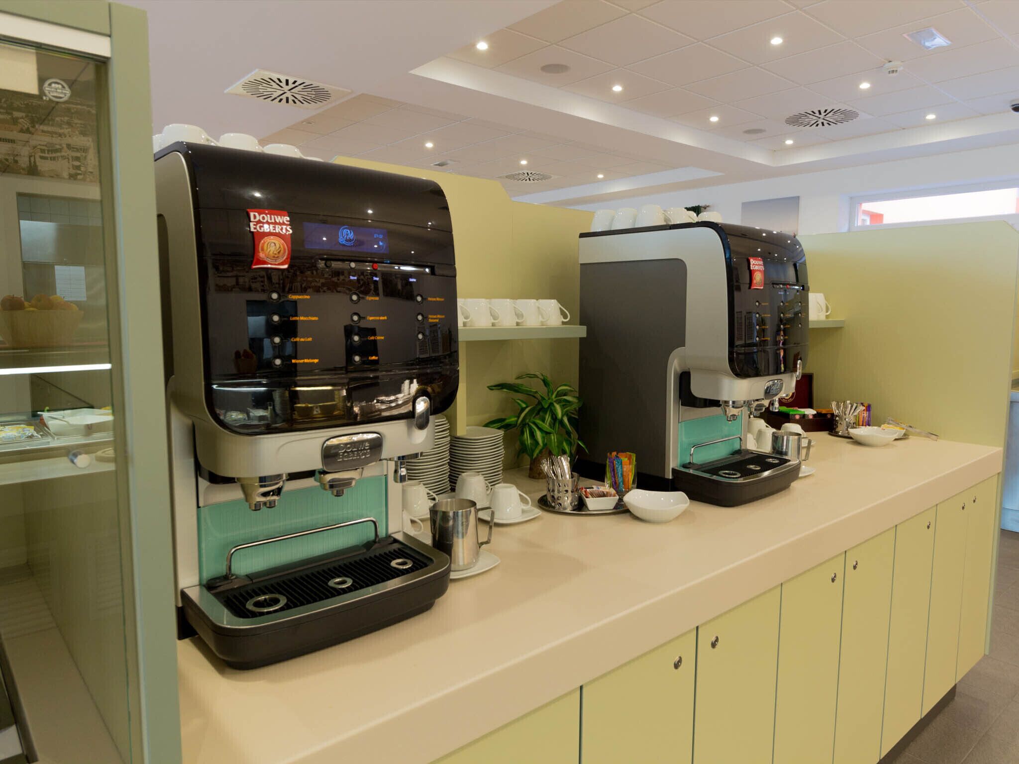 Una estación de café con dos máquinas de espresso, un expositor de vidrio y una planta.