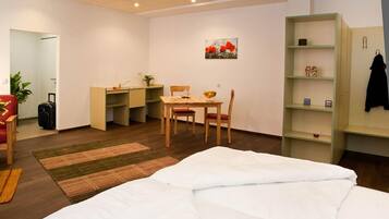 A hotel room with a bed, a desk, a chair, a small table, a bookshelf, and a painting on the wall.