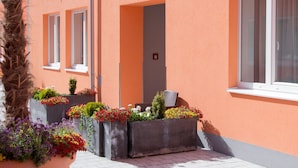 A building with a peach exterior, a door, and windows. There are flower planters in front of the building. - Winrooms (Wiener Neustadt)