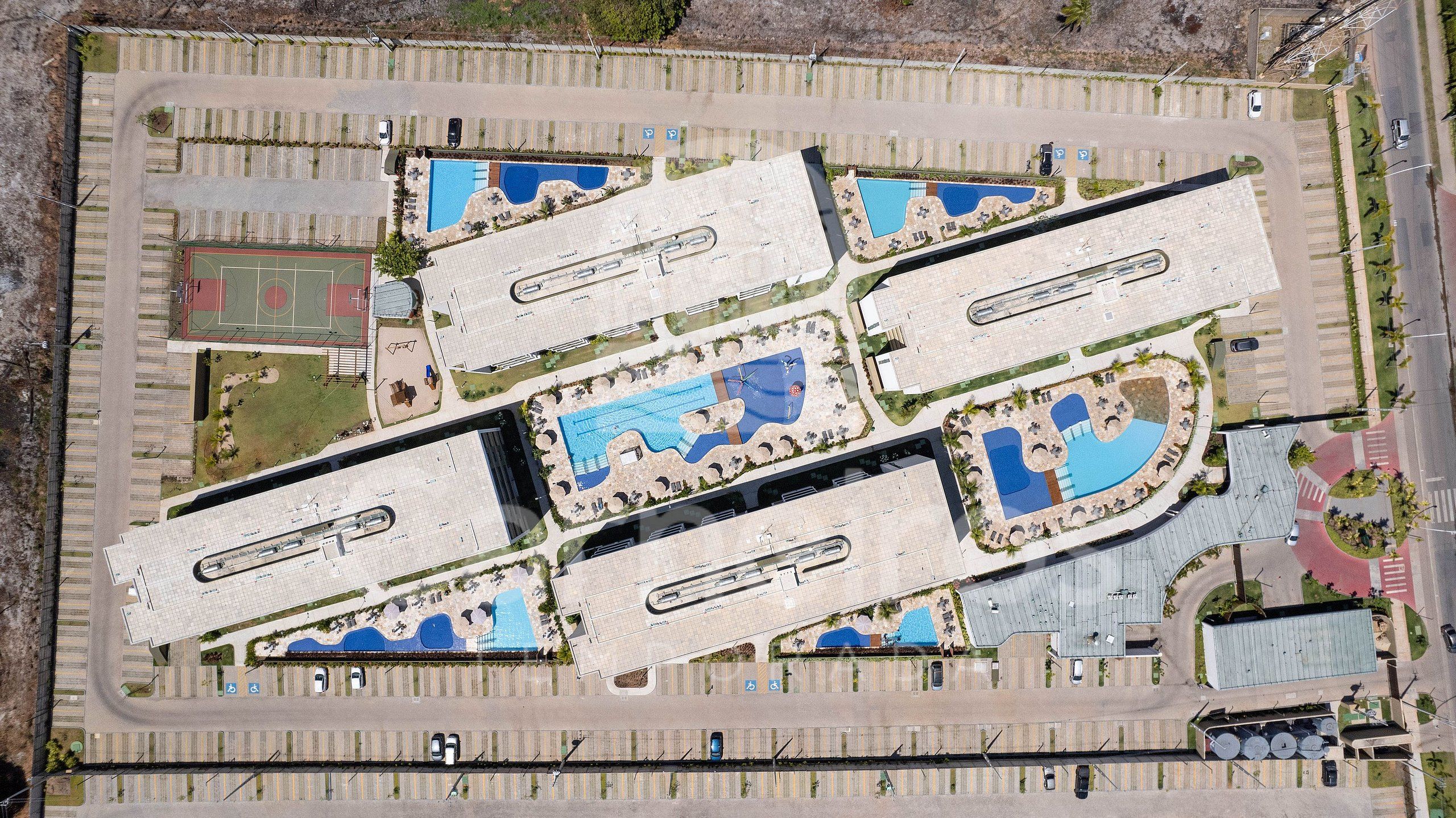 Vogelperspektive eines Komplexes mit mehreren Schwimmbecken, Parkplätzen und einem Sportplatz.