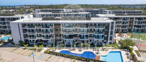 A modern multi-story hotel with a swimming pool, outdoor seating, and a view of the ocean.