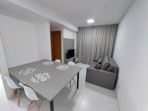 A modern living space with a dining table, chairs, a sofa, and a TV. - Mana Beach Experience- Porto de Galinhas (Ipojuca)