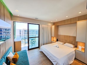 Una habitación de hotel moderna con una cama grande, un sofá, un balcón con vistas a edificios y una puerta corrediza de vidrio.