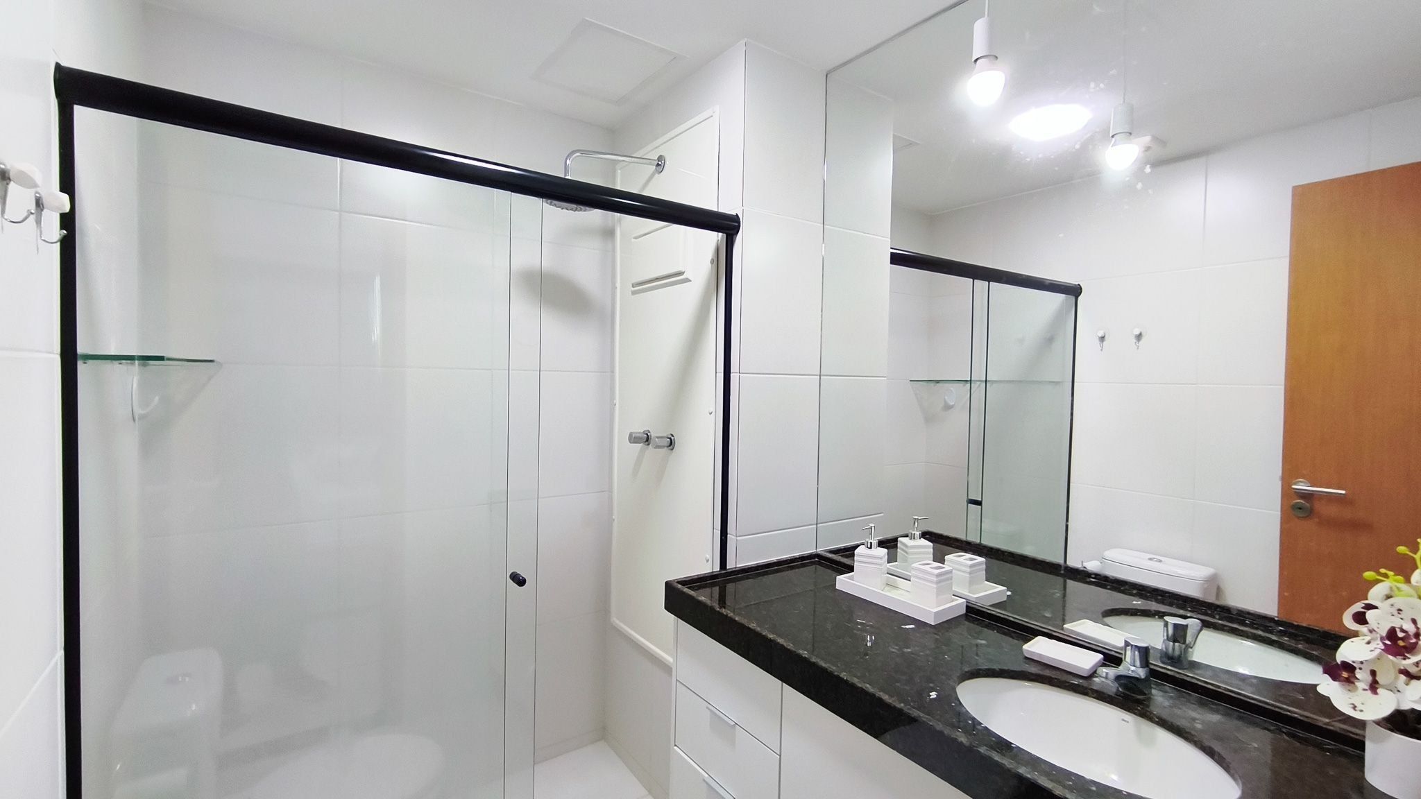 Een moderne badkamer met een douchecabine van glas, een zwart aanrecht en een grote spiegel.