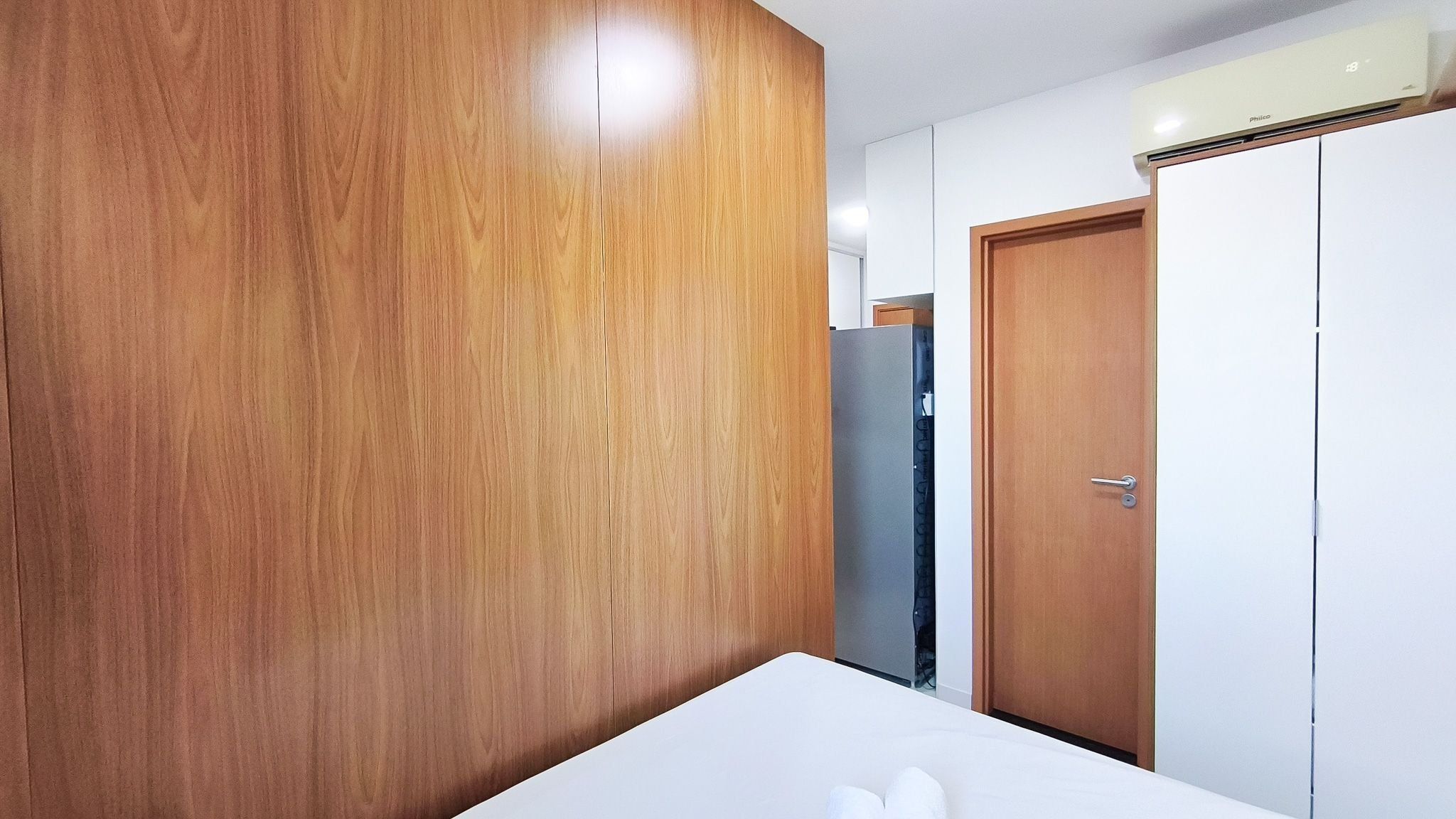 A room with a wooden wardrobe, a white bed, and a closed door.