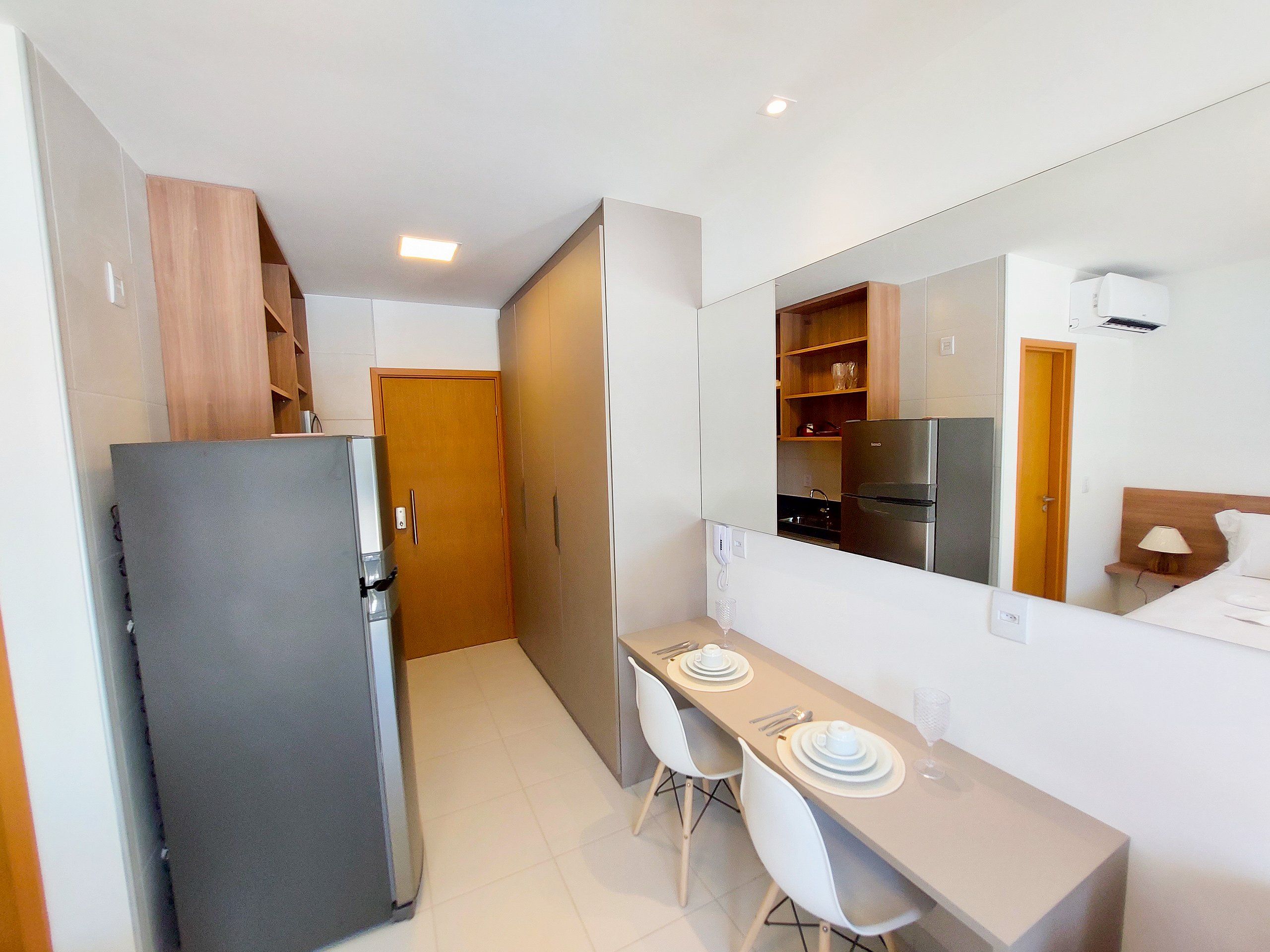 A compact hotel room with a kitchenette, a dining area, and a large mirror.