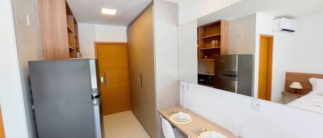 A compact hotel room with a kitchenette, a dining area, and a large mirror.