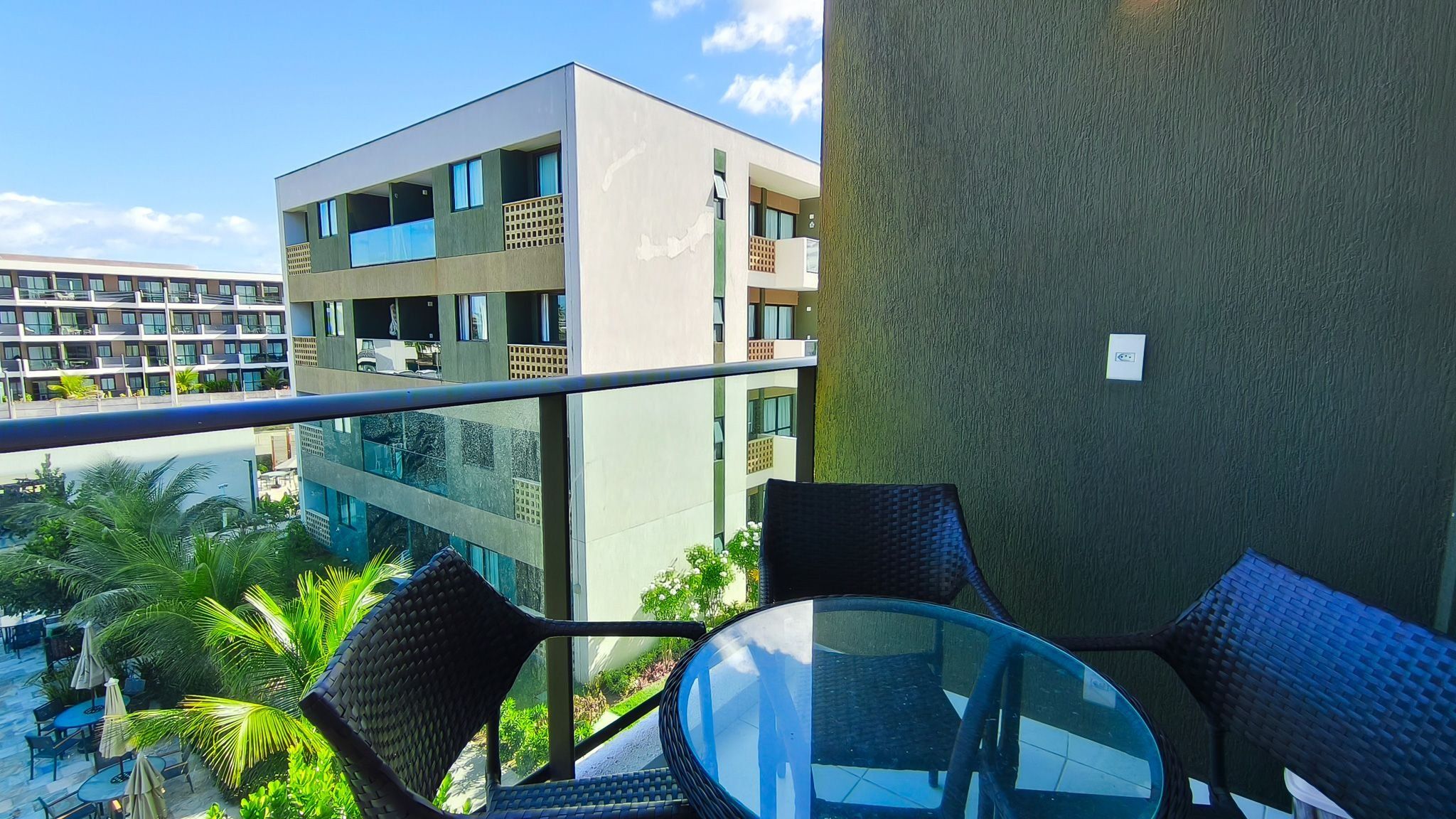 A balcony with a glass table and chairs, overlooking a modern building with multiple floors and balconies.