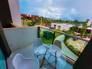 A balcony with two white chairs and a table, overlooking a residential area with houses and greenery. - Mana Beach Experience- Porto de Galinhas (Ipojuca)