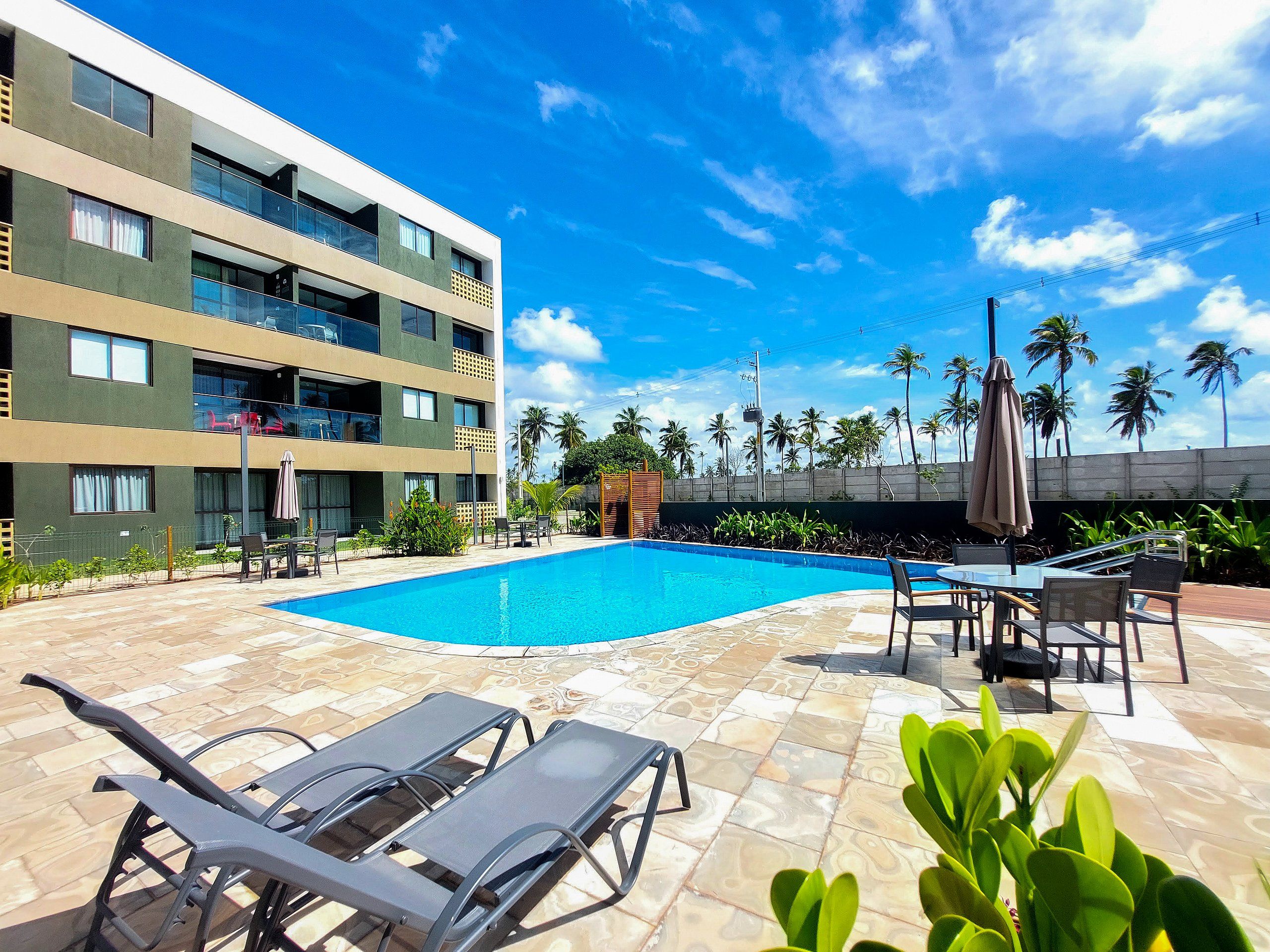 A hotel with a swimming pool, outdoor seating, and a view of palm trees.