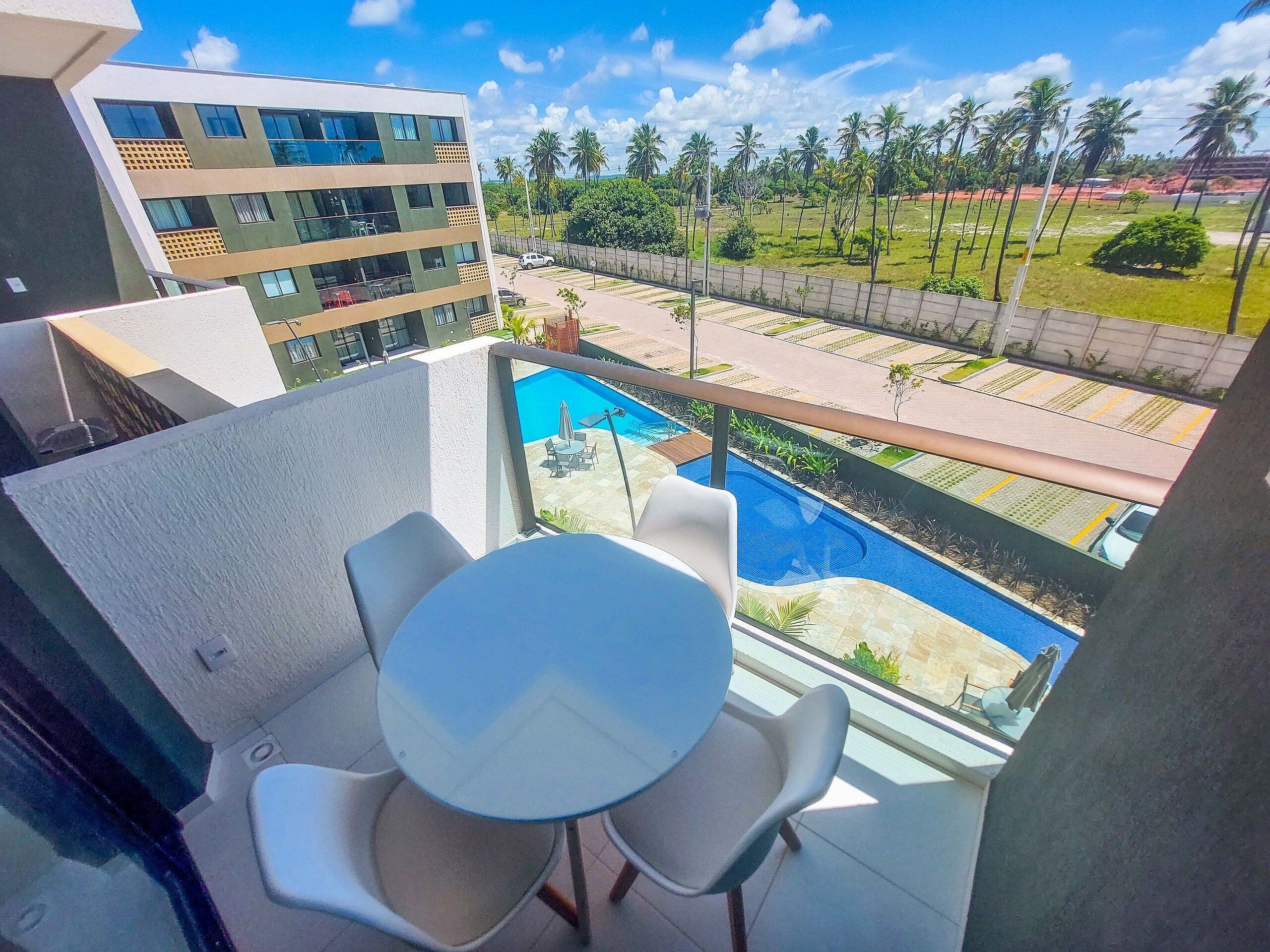 A balcony with a pool, chairs, and a view of a building and palm trees.