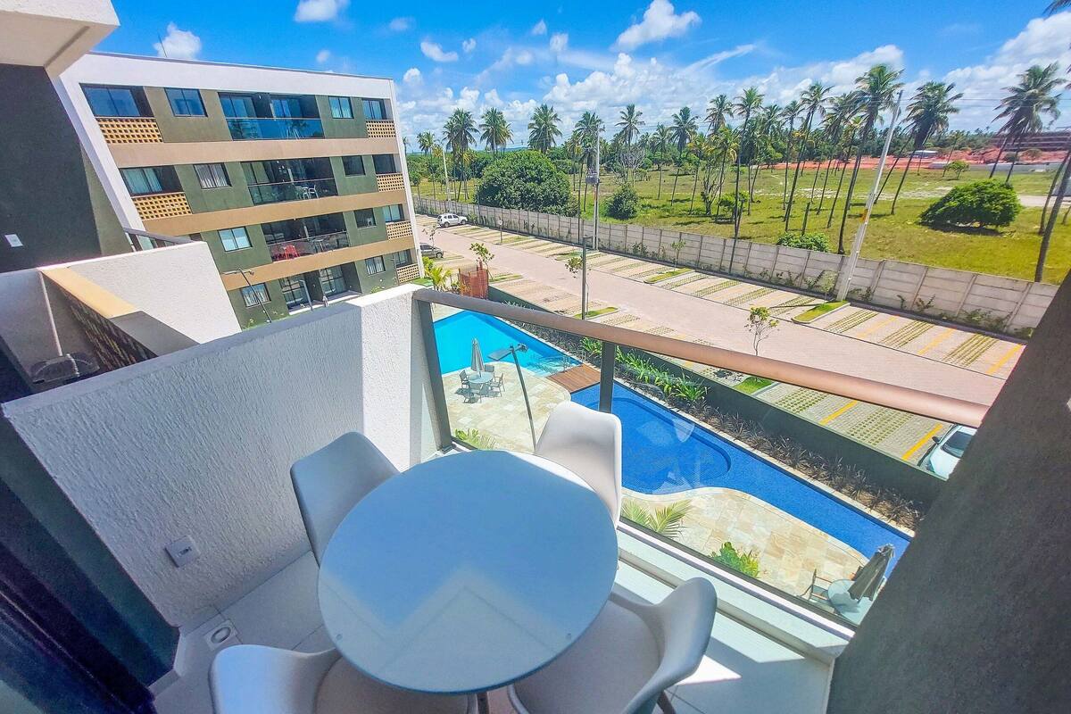 Varanda com piscina, cadeiras e vista para um edifício e palmeiras.