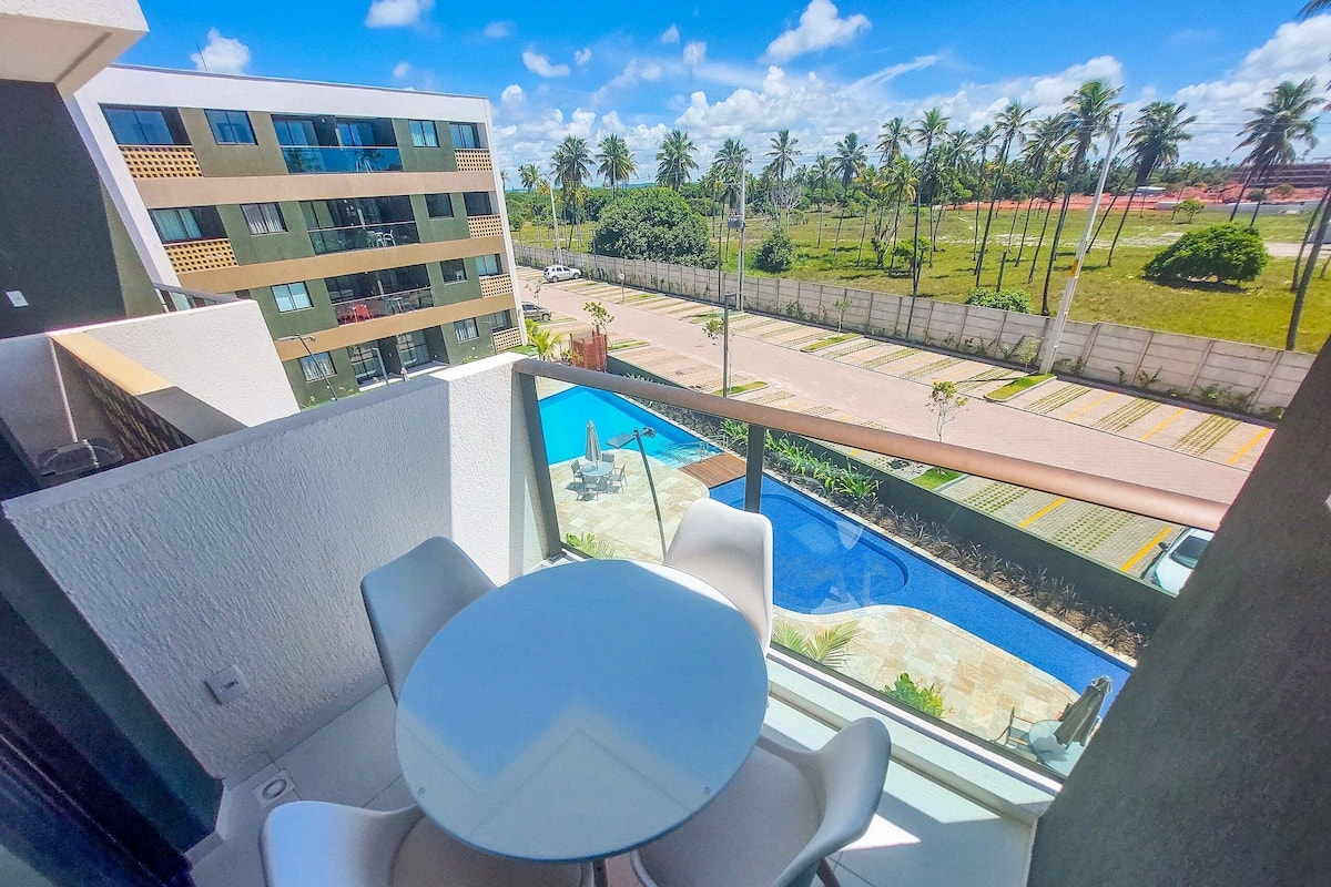 A balcony with a pool, chairs, and a view of a building and palm trees.