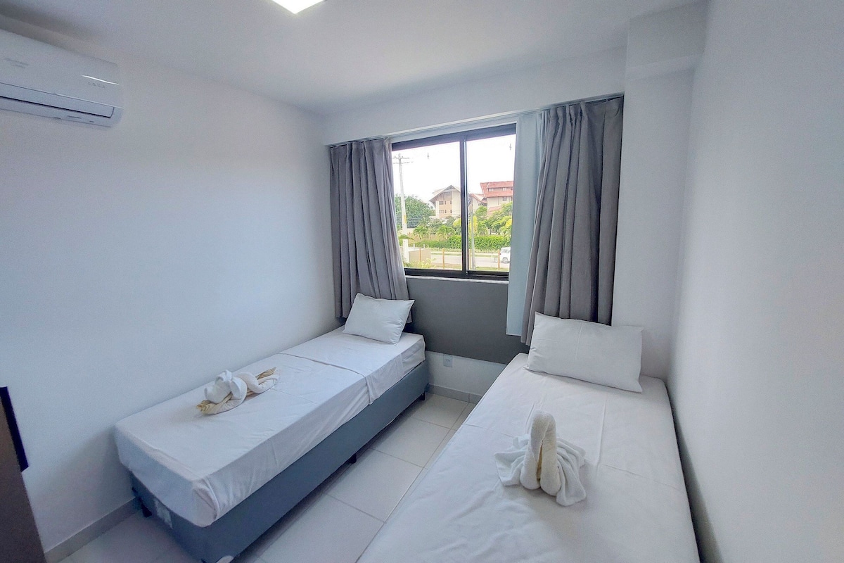 Quarto de hotel pequeno com duas camas, uma janela com cortinas, ar condicionado visível e vista para prédios.