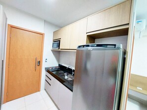 A compact kitchen with a refrigerator, microwave, and a wooden door. - Mana Beach Experience- Porto de Galinhas (Ipojuca)