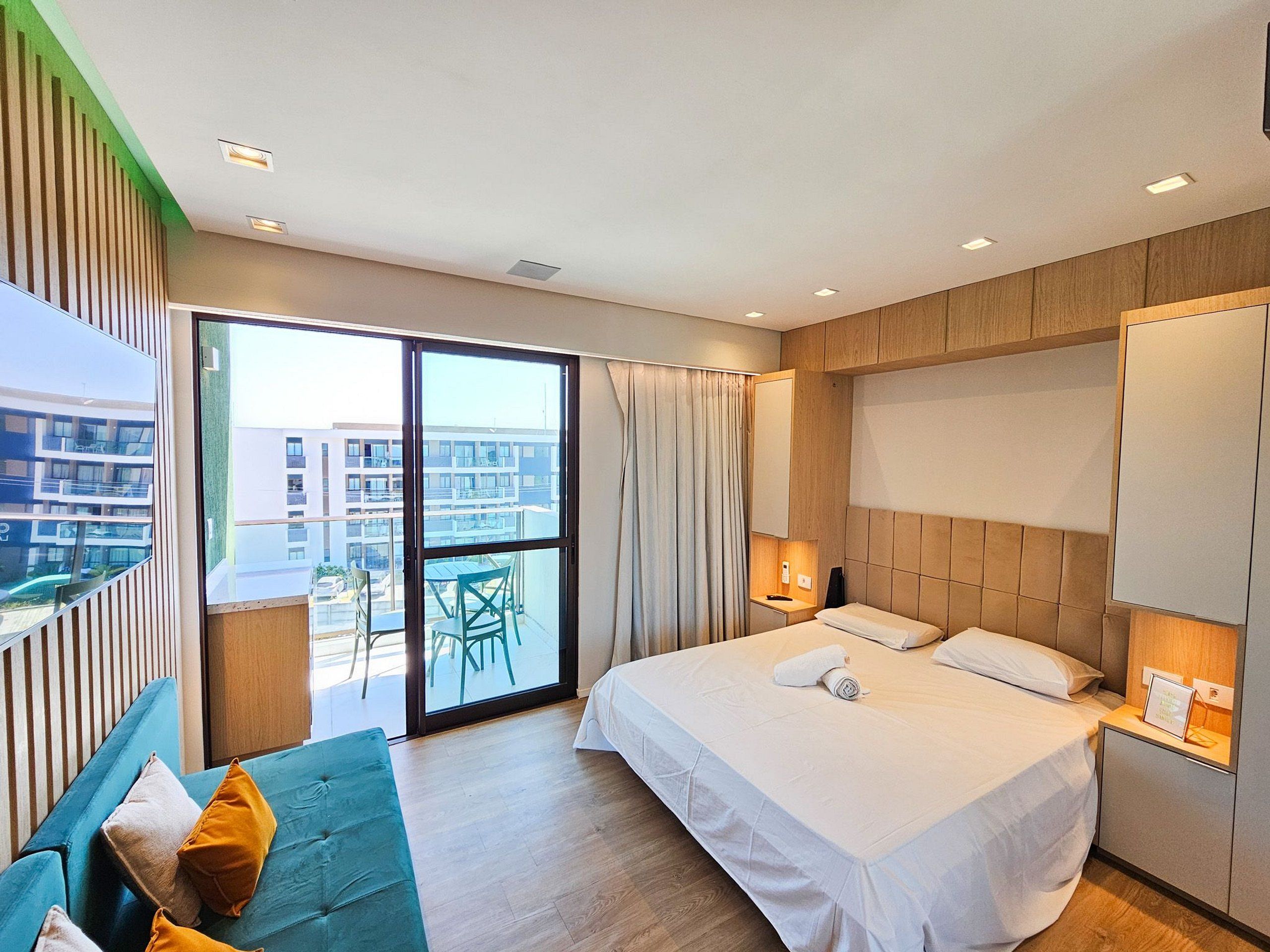 Quarto de hotel moderno com uma cama grande, um sofá, uma varanda com vista para edifícios e uma porta de correr de vidro.