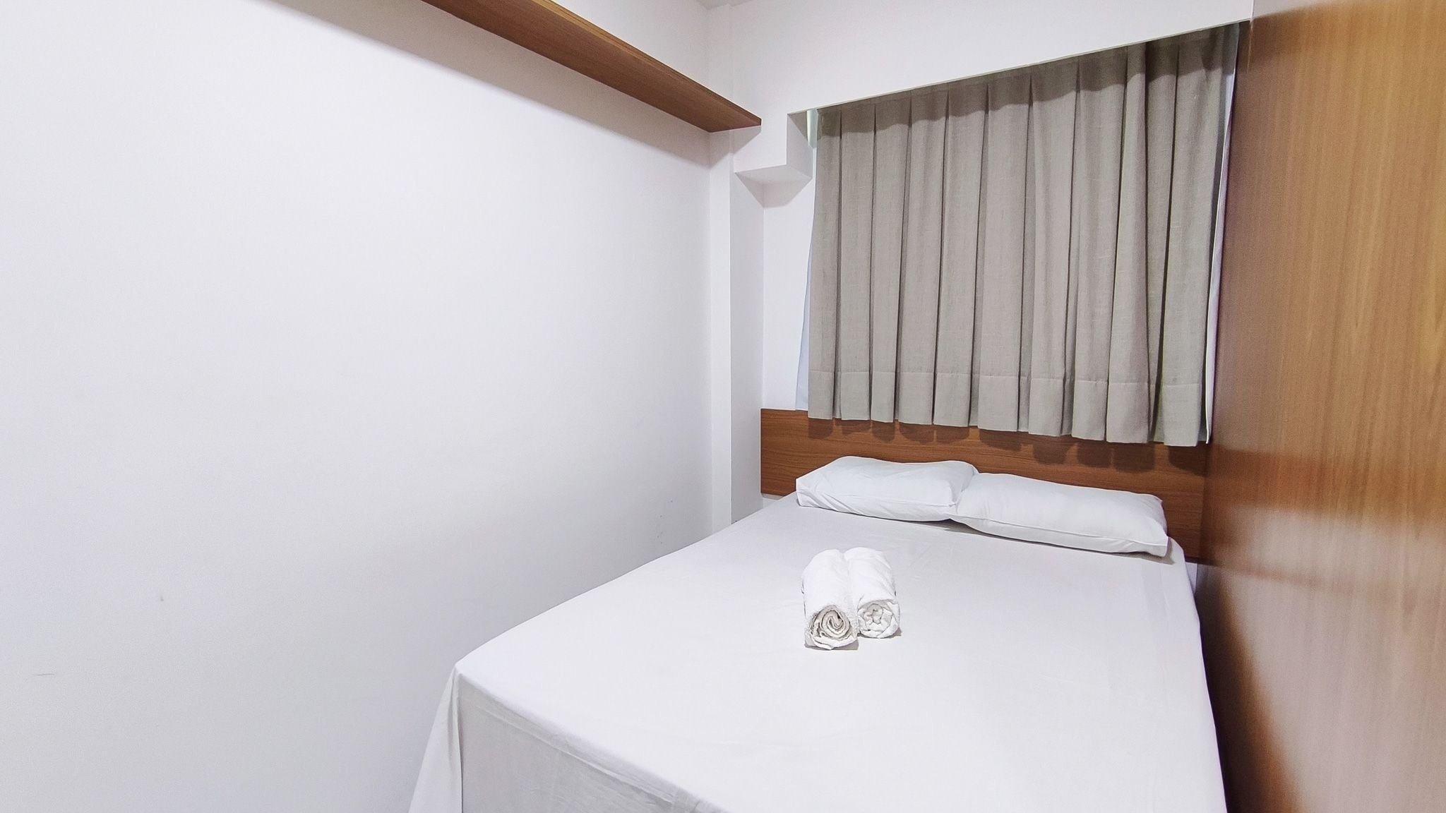 A single bed with a wooden headboard, white bedding, and a pair of shoes on the bed.