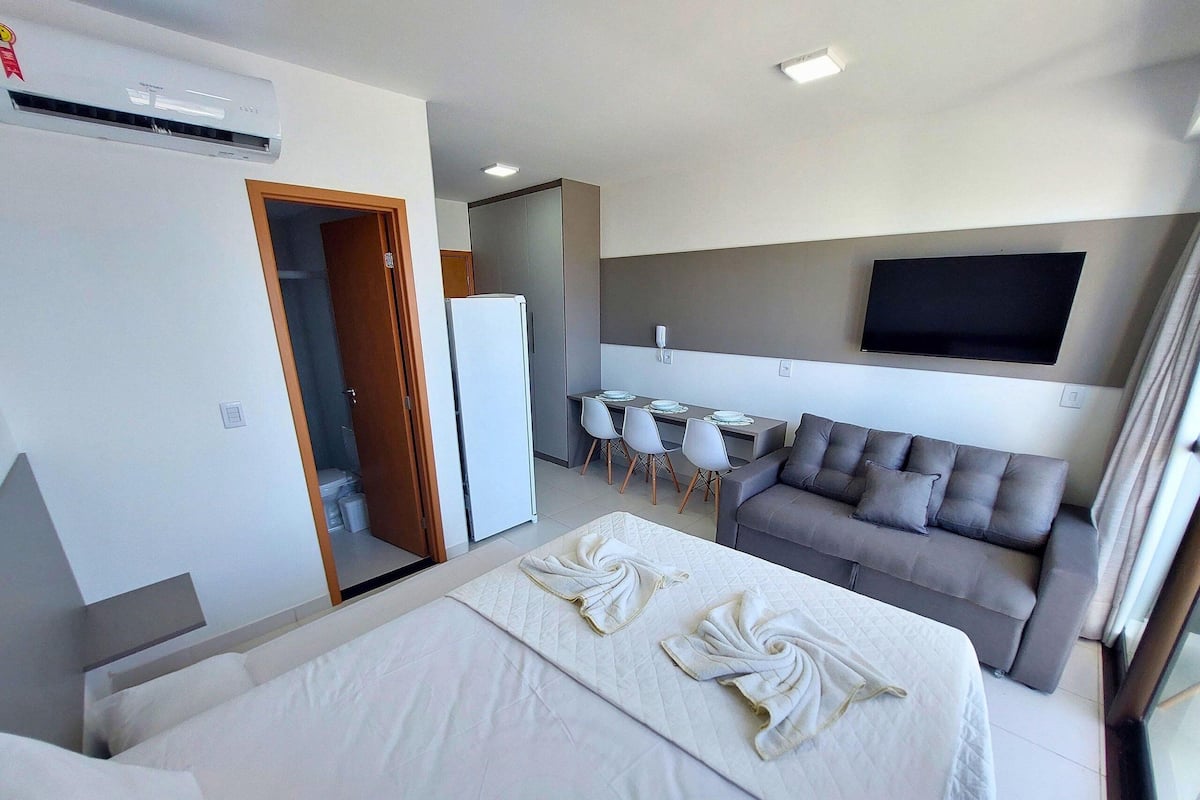 Quarto de hotel com cama, sofá, área de refeições e televisão.