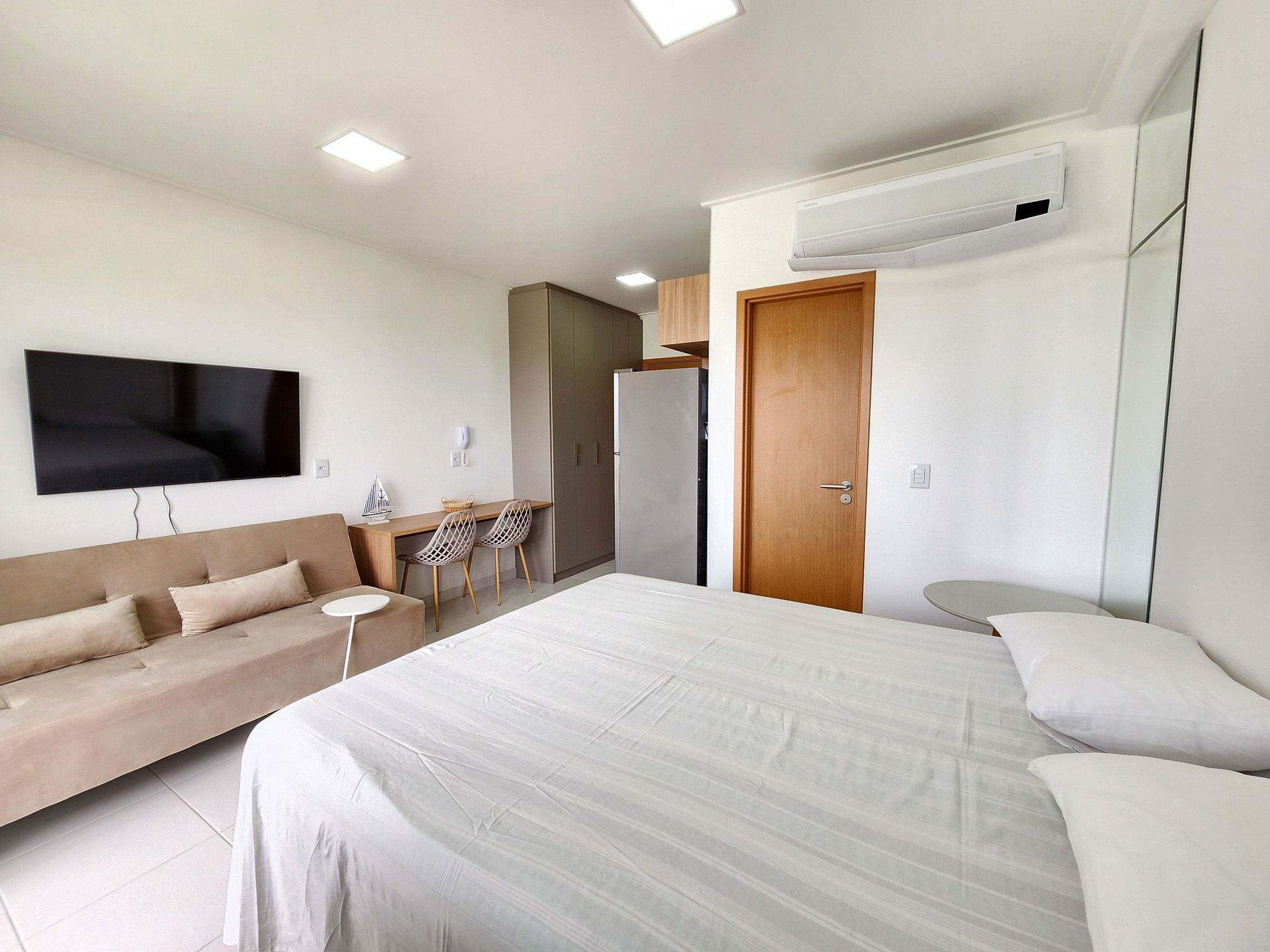 Habitación de hotel moderna con cama, sofá, escritorio, televisor, aire acondicionado y armario.