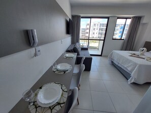 A hotel room with a dining area, a bed, and a view of buildings. - Mana Beach Experience- Porto de Galinhas (Ipojuca)