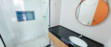 A bathroom with a glass-enclosed shower, a white toilet, a sink with a black countertop, and a round mirror with an orange frame.