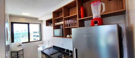 A kitchen with a stainless steel refrigerator, a microwave, and a red blender on the countertop.