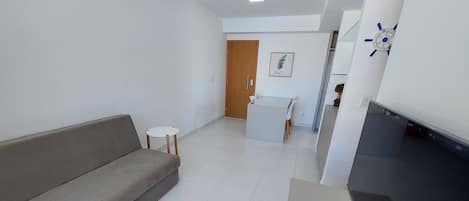 A modern living room with a sofa, a small table, a dining area, and a kitchen area with a black countertop.