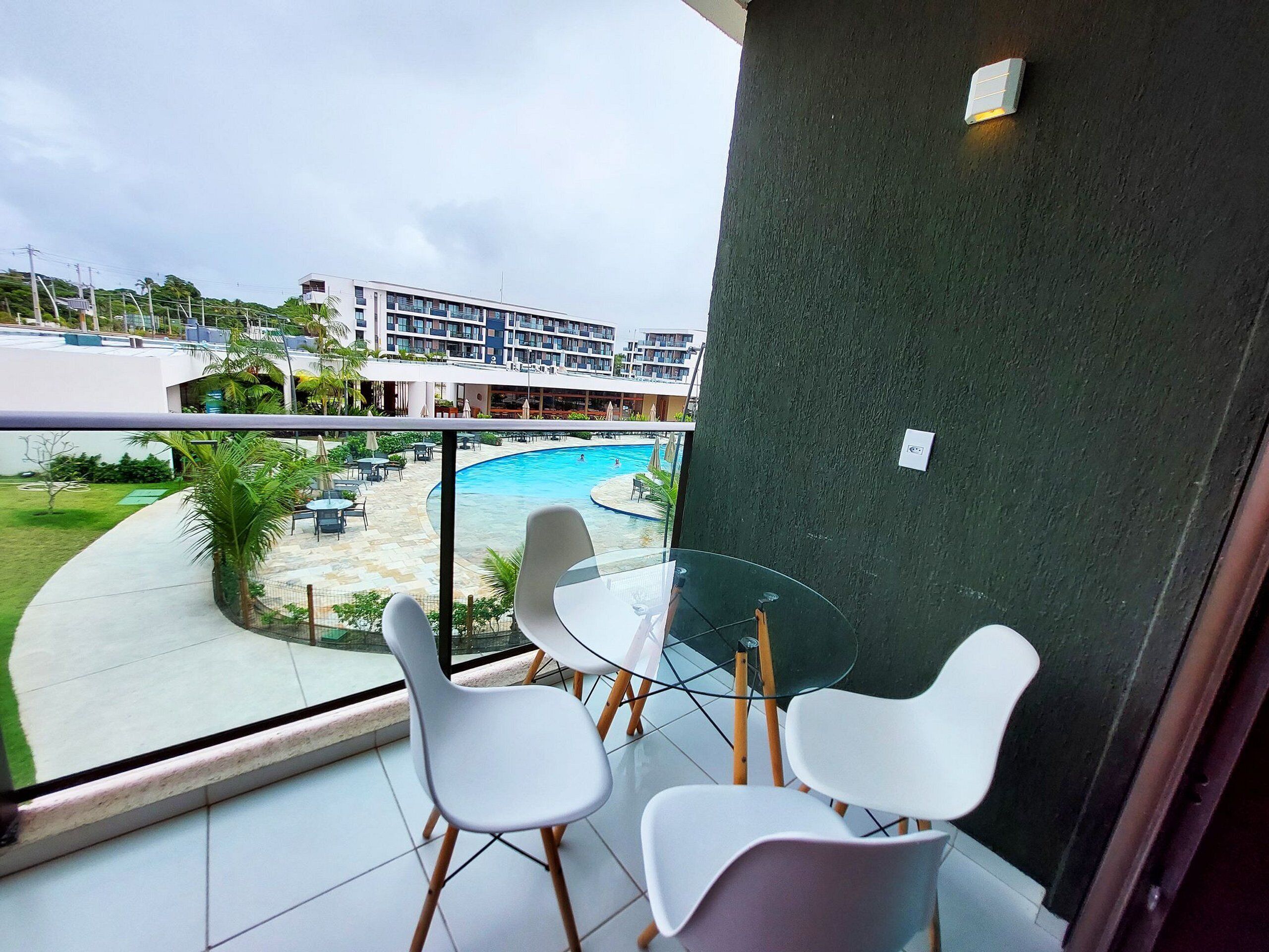 A balcony with a glass table and chairs, overlooking a swimming pool and a hotel building.