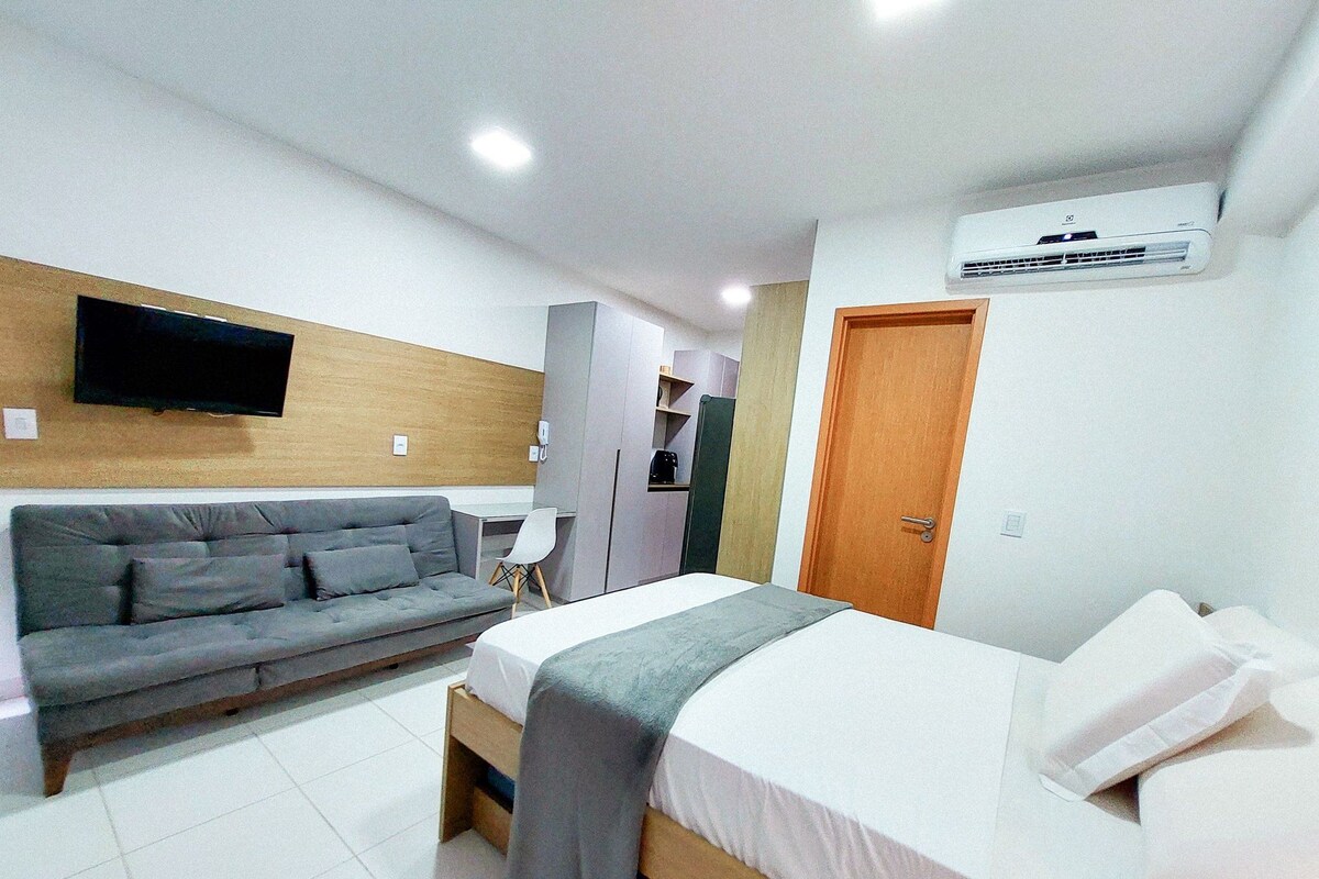 A modern hotel room with a bed, a sofa, a TV, and an air conditioning unit.